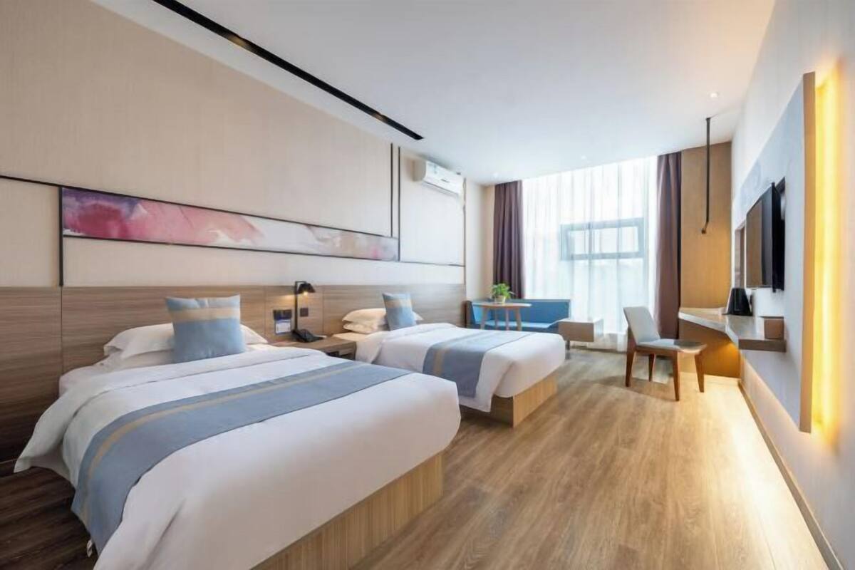 A modern hotel room with two beds, a desk, a chair, and a large window.