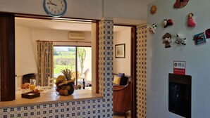 A room with patterned tile walls, a wooden-framed window, a clock, and a wall-mounted phone.