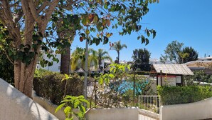 A pool area with a white fence, a tree, and a building with a tiled roof in the background.