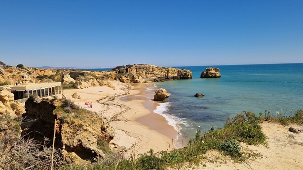 A coastal beach with rocky formations, clear blue water, and a small boat in the distance.