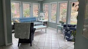A sunlit room with a ceiling fan, a blue sofa, a patterned chair, and a view of the outside through large windows. - Classic mid-century Long Beach home with modern updates - Walk to Stop 30 beach! (Long Beach)