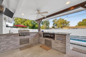 An outdoor kitchen with a grill, a built-in oven, and a ceiling fan.