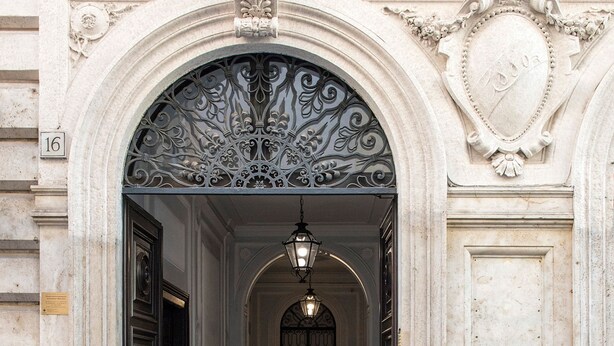 An ornate entrance with a grand archway, a metal door, and a tiled floor leading into a hallway. - Alta Luxury Apartments - Spagna Apartment (Rome)