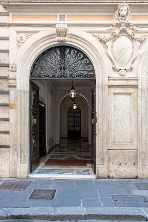An ornate entrance with a grand archway, a metal door, and a tiled floor leading into a hallway. - Alta Luxury Apartments - Spagna Apartment (Rome)