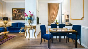 A modern living room with a blue sofa, a dining table with blue chairs, a gold-framed mirror, and a painting on the wall. - Alta Luxury Apartments - Spagna Apartment (Rome)