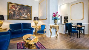 A spacious living room with a blue sofa, a coffee table, and a large painting on the wall. - Alta Luxury Apartments - Spagna Apartment (Rome)