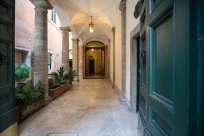 A corridor with columns, a green door, and potted plants. - Alta Luxury Apartments - Frezza Apartment (Rome)