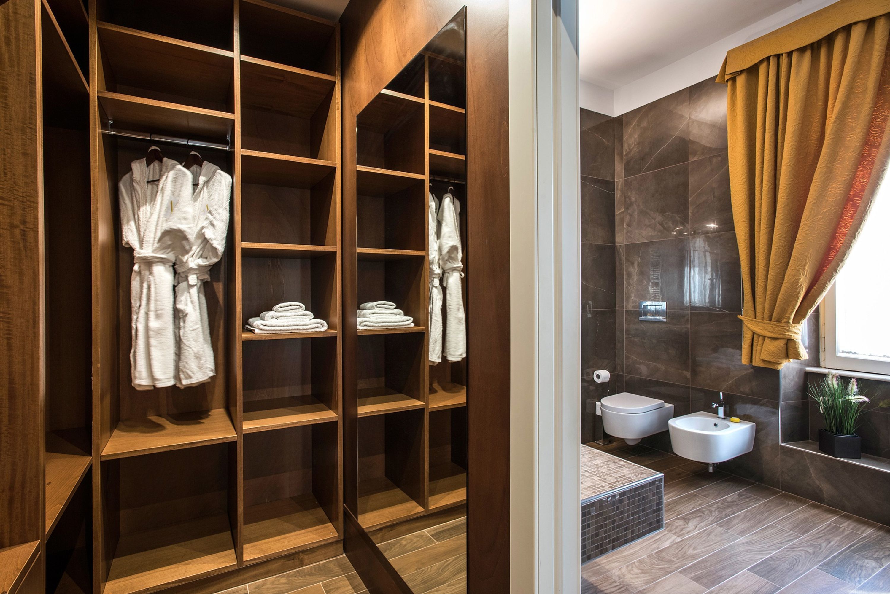 A modern bathroom with a walk-in shower, a bidet, a sink, and a wooden robe closet with towels.