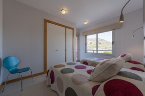 A bedroom with two beds, a blue chair, and a large window with a view of a hilly landscape. - Villa in Maspalomas With Heated Pool & Golf Views (San Bartolomé de Tirajana)