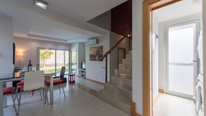 A modern living room with a dining area, a staircase, and a large window.