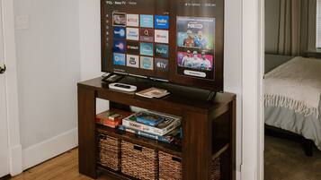 Un téléviseur posé sur un meuble en bois, avec une télécommande, un livre et une console de jeux à proximité.