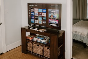 Un televisor sobre un soporte de madera con un control remoto, un libro y una consola de videojuegos.