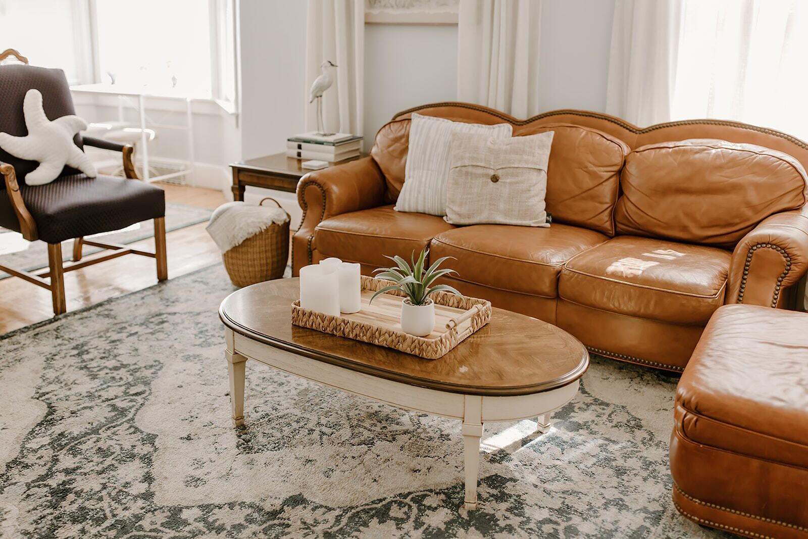 A cozy living room with a brown leather sofa, a matching ottoman, a wooden coffee table, and a decorative basket.