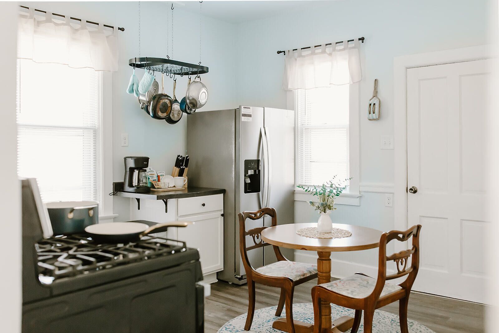 Una cocina con estufa a gas, refrigerador, mesa de comedor con sillas y un colgador para ollas.