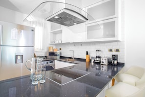 A modern kitchen with a central island, stainless steel appliances, and a white tiled backsplash. - Cana Rock Condos (Punta Cana)