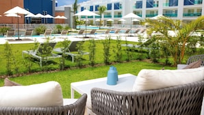 A pool area with lounge chairs and umbrellas, a white table with a blue vase, and a building with multiple balconies. - Cana Rock Condos (Punta Cana)