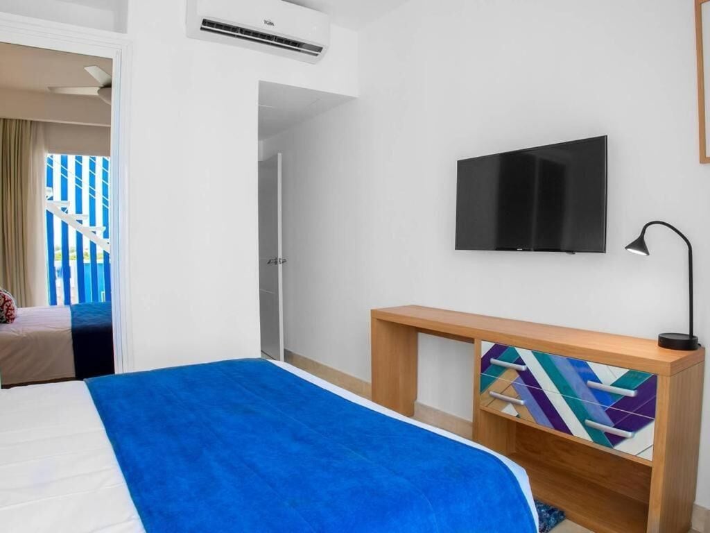 Une chambre d’hôtel avec un lit, une télévision, un bureau et une fenêtre donnant sur des bâtiments bleus.