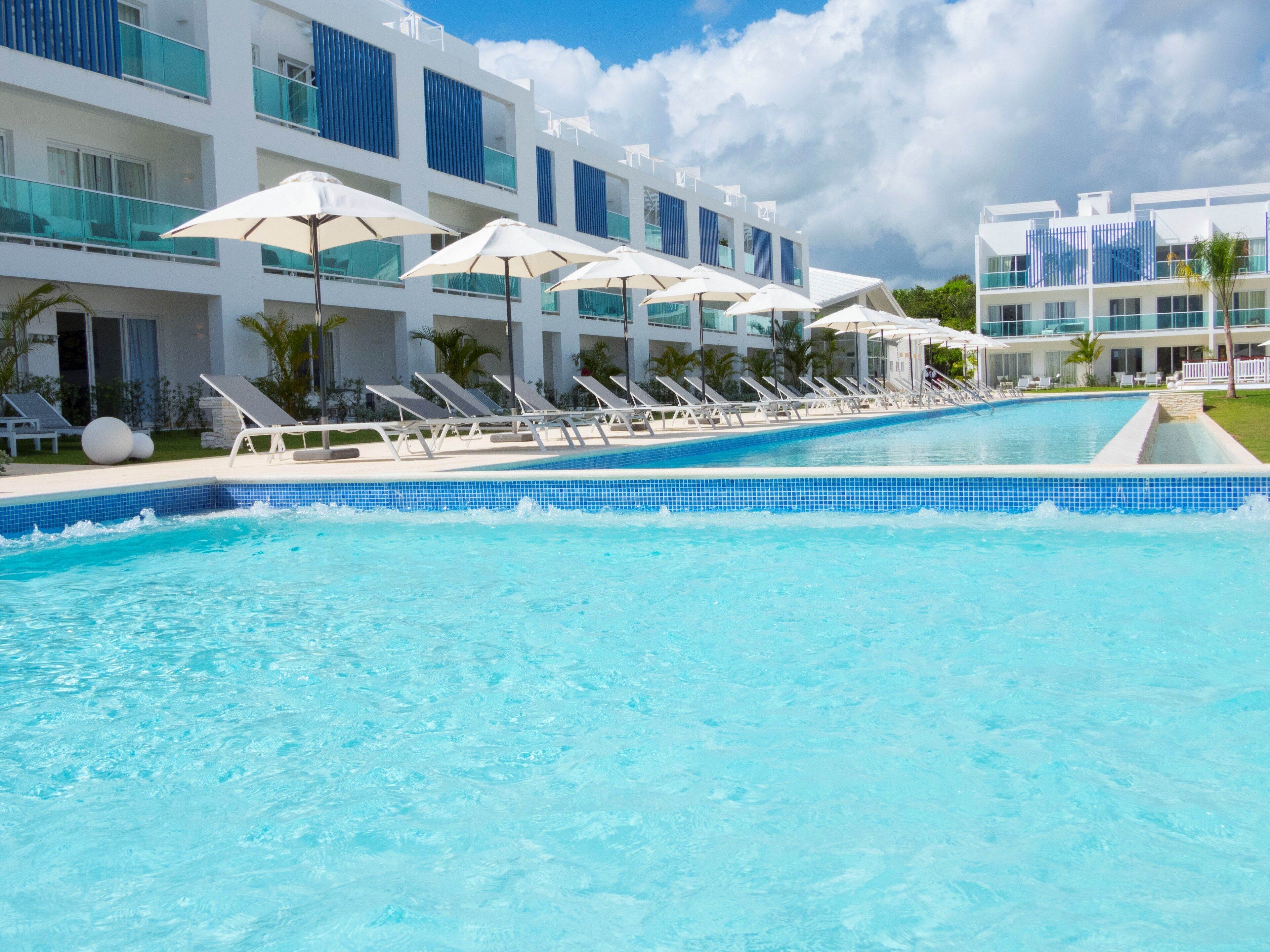 A swimming pool with lounge chairs and umbrellas, surrounded by modern buildings with balconies.