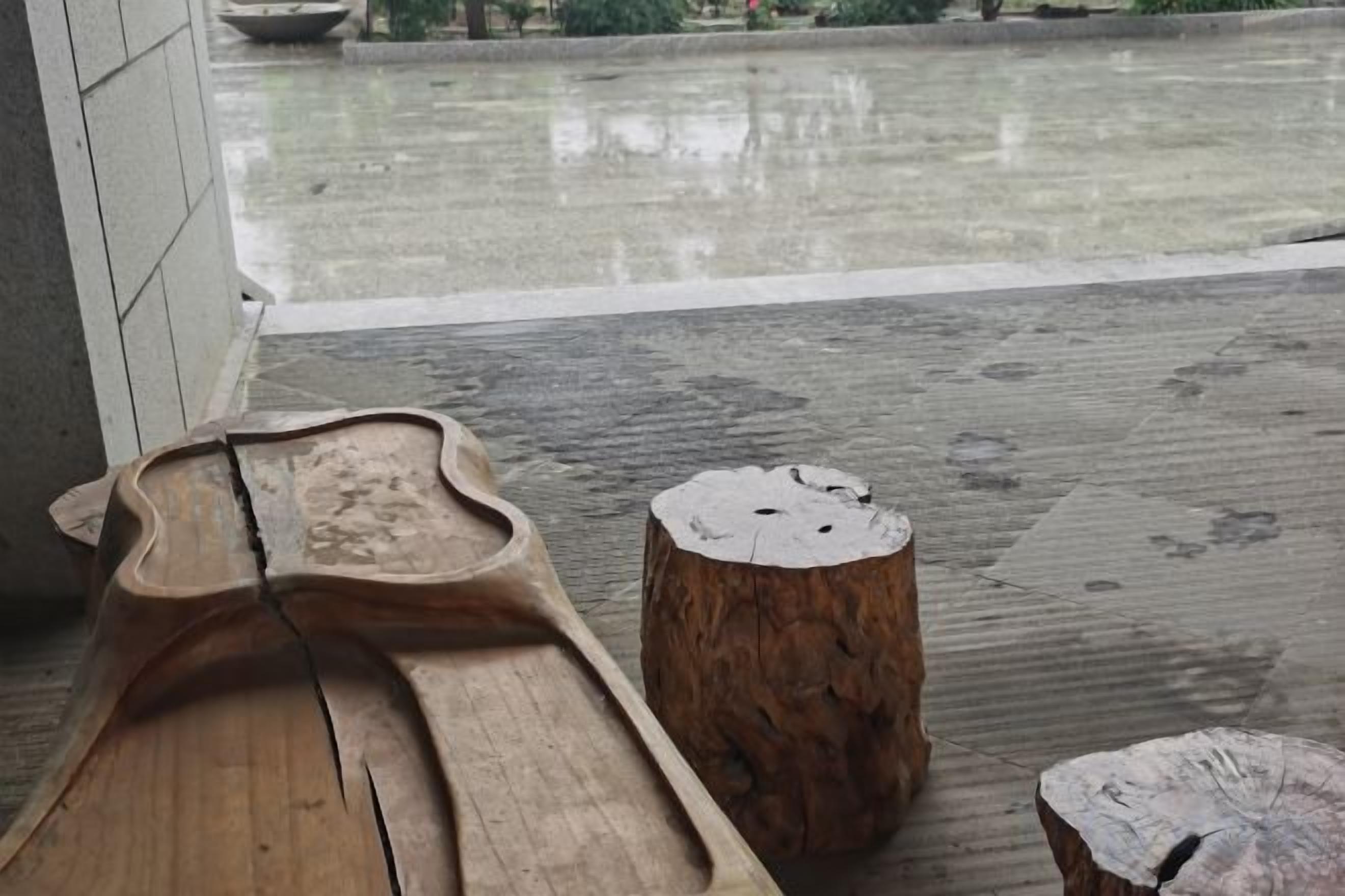 A wooden bench and two tree stump stools on a concrete floor with a wet surface.
