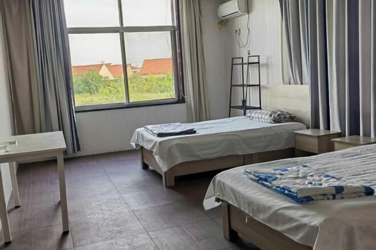 Une chambre d’hôtel avec deux lits, un bureau, une étagère et une fenêtre avec des rideaux.