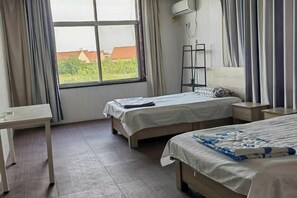 Habitación de hotel con dos camas, un escritorio, una estantería y una ventana con cortinas.