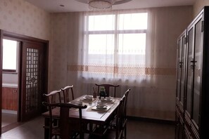 Comedor con mesa para cuatro, ventana con cortinas de encaje y muebles de madera tradicionales.