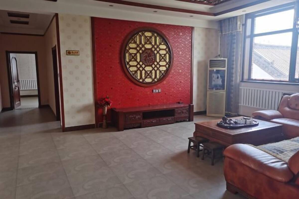 Une chambre d’hôtel avec un mur d’accent rouge, une fenêtre ronde décorative, un canapé en cuir et une petite table.