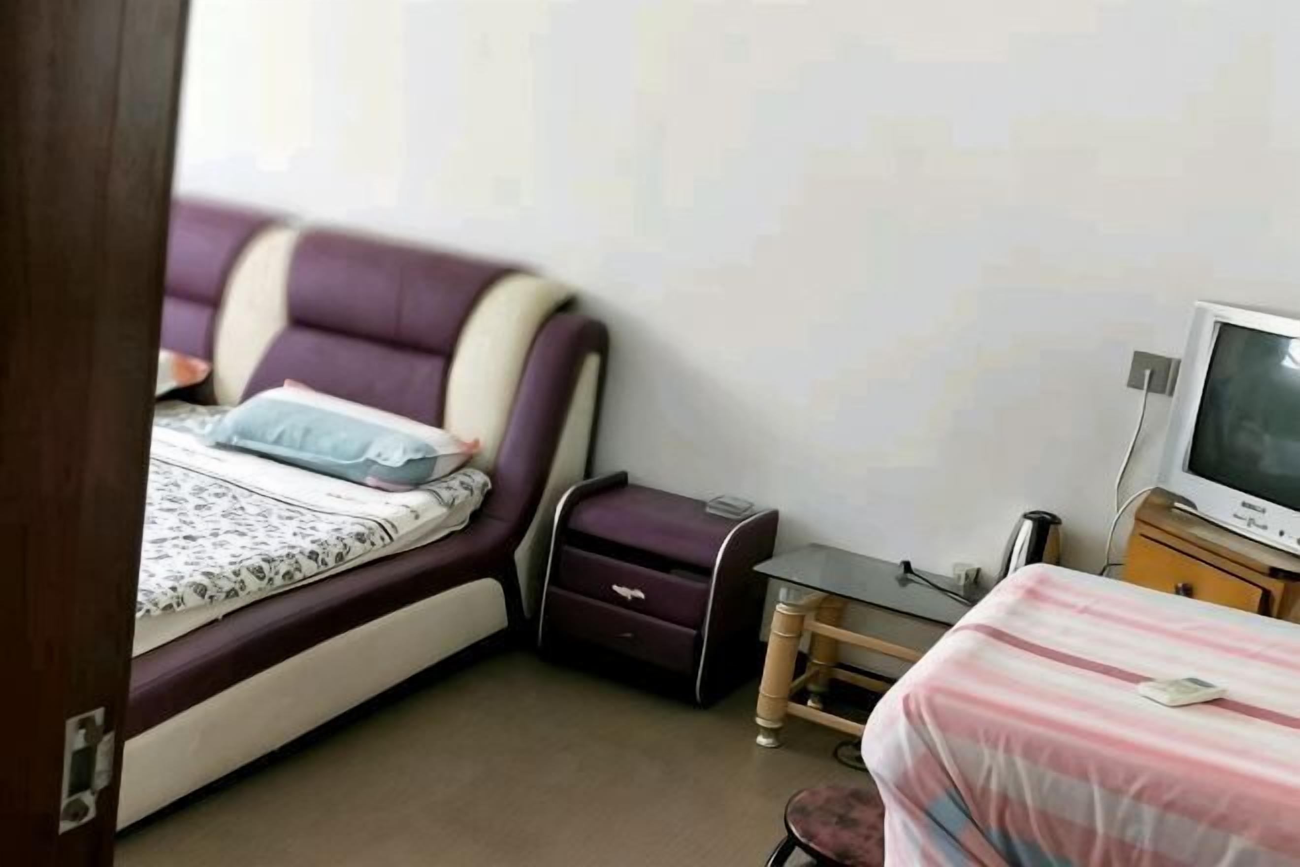 Um quarto com uma cama, uma televisão, uma mesinha e uma cadeira.