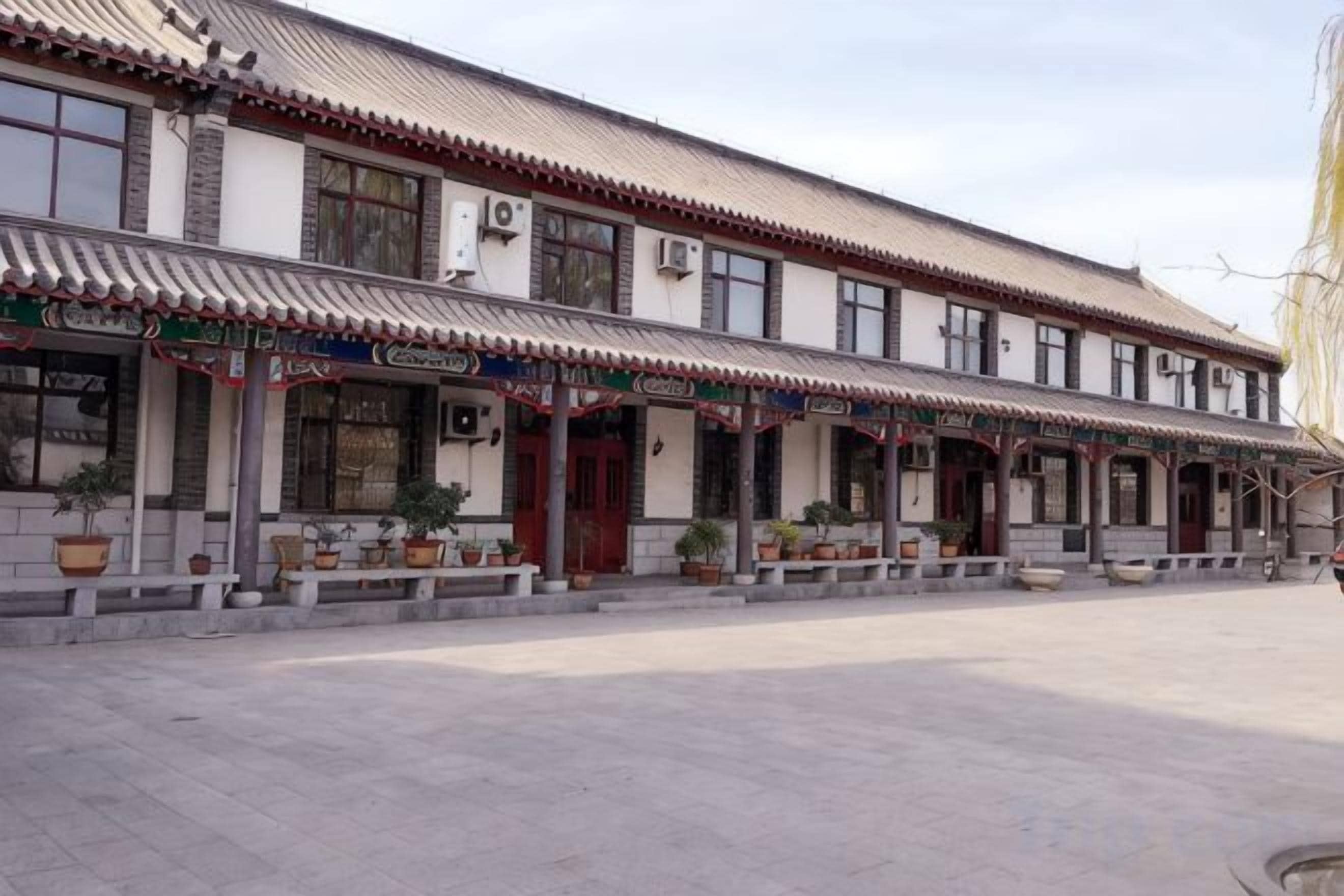 A traditional building with a tiled roof, multiple windows, and a covered walkway with potted plants.