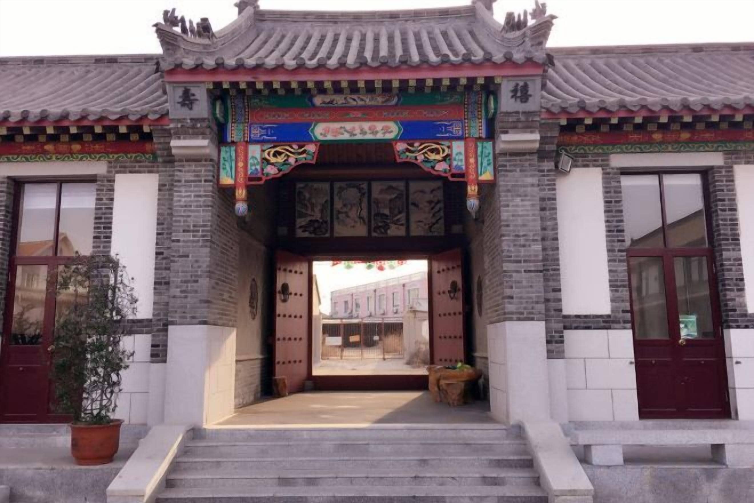 A traditional Chinese building entrance with a tiled roof, a decorative archway, and a staircase leading to the entrance.