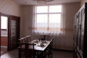 Un comedor con una mesa dispuesta para cuatro personas, sillas, un armario y una ventana con cortinas de encaje.