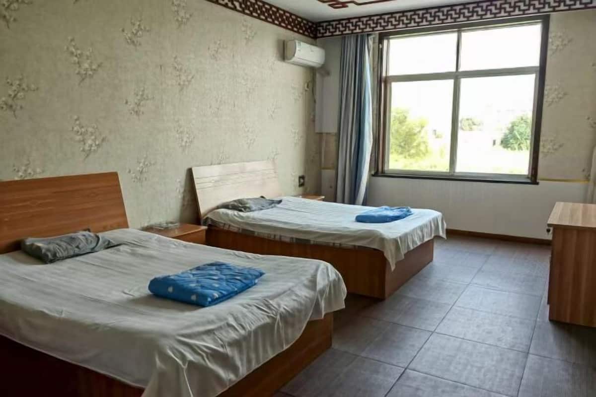 Une chambre avec deux lits, une fenêtre avec des rideaux et un bureau en bois.