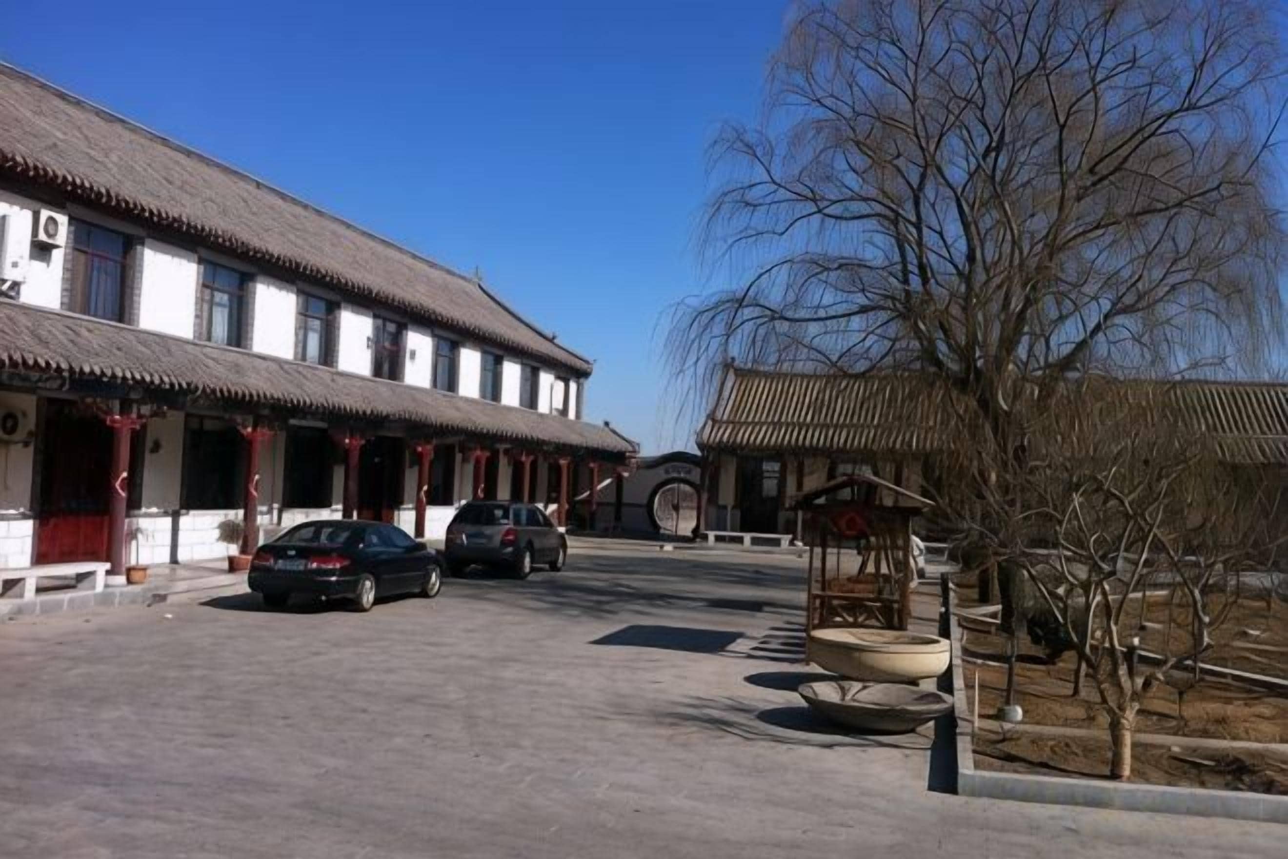 A traditional building with a tiled roof, a courtyard, and parked cars.