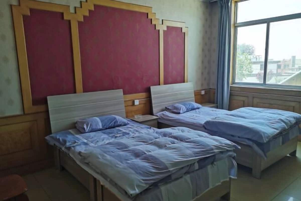 Une chambre avec deux lits, une fenêtre avec des rideaux et un mur orné d’un panneau décoratif.