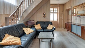 Una sala de estar con un sofá de cuero negro, una mesita, un armario de madera y una escalera.