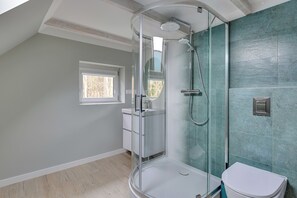Un baño moderno con ducha envuelta en vidrio, inodoro y una ventana pequeña.