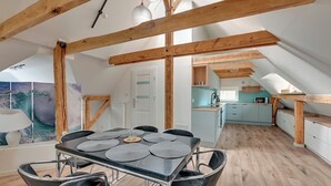 Un comedor con una mesa dispuesta para seis comensales, vigas de madera y vista a una cocina.