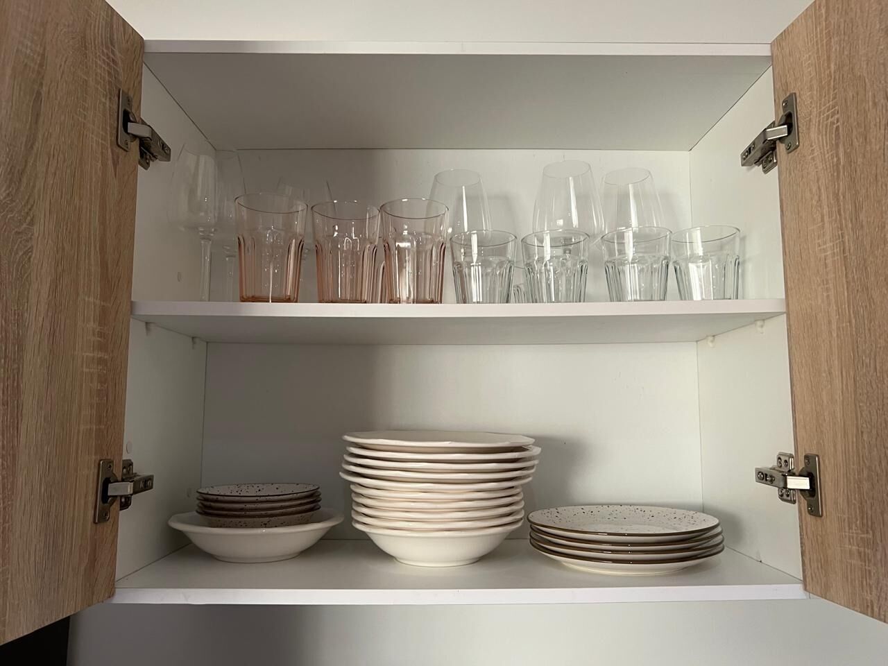 Un meuble avec deux étagères ; l’étagère supérieure contient de la verrerie transparente, et l’étagère inférieure est remplie d’assiettes et de bols empilés.