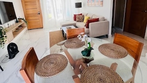 Ein modernes Wohnzimmer mit einem Glastisch, Holzstühlen und einer außergewöhnlichen Pendelleuchte aus Holz.