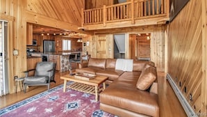 Interior espacioso de una cabaña con detalles de madera, una sala de estar con sofá de cuero, una mesa de comedor y una cocina con electrodomésticos modernos.