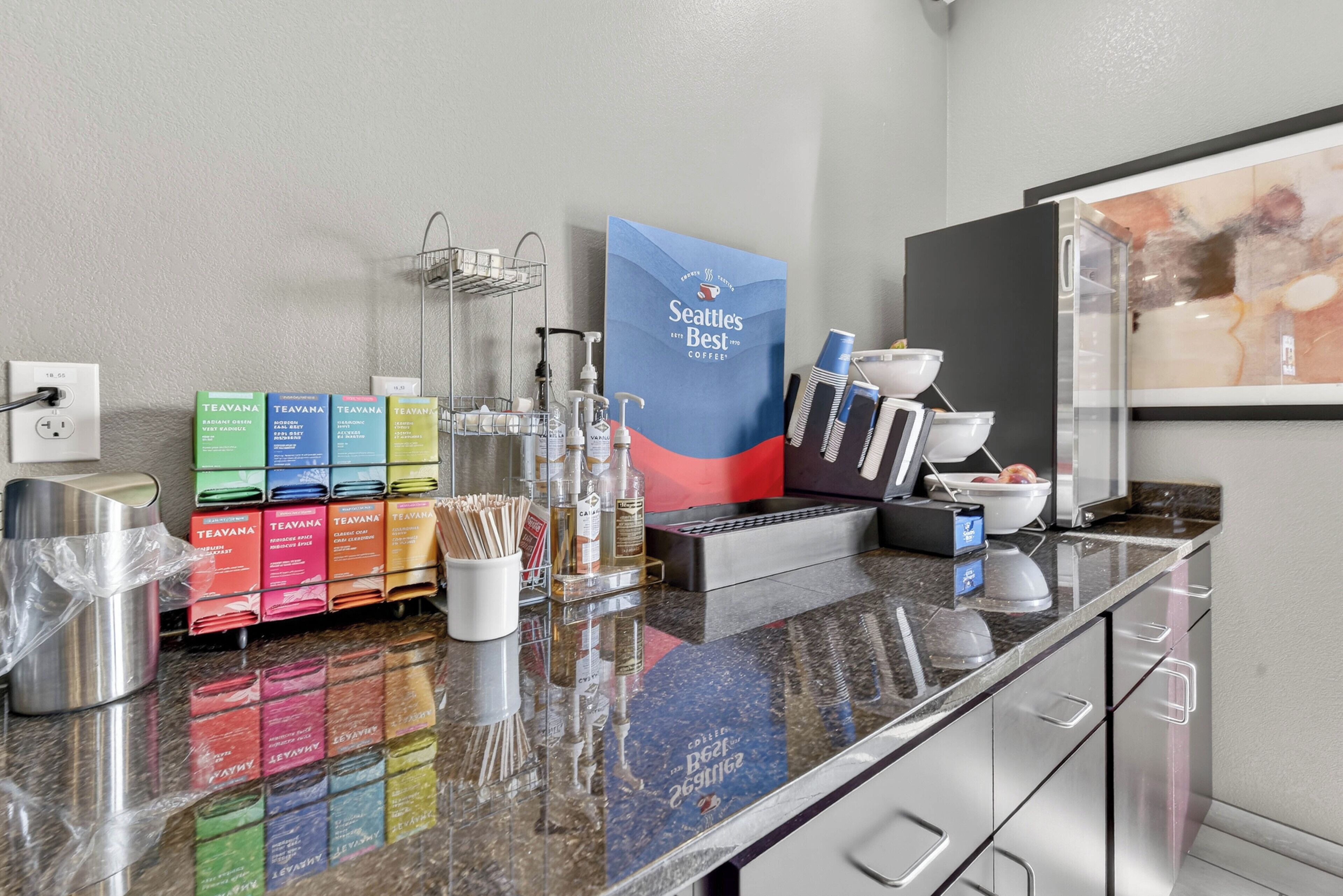 Un espace dédié au petit-déjeuner dans l’hôtel, comprenant un coin café, des distributeurs de thé et un présentoir de sachets de café.