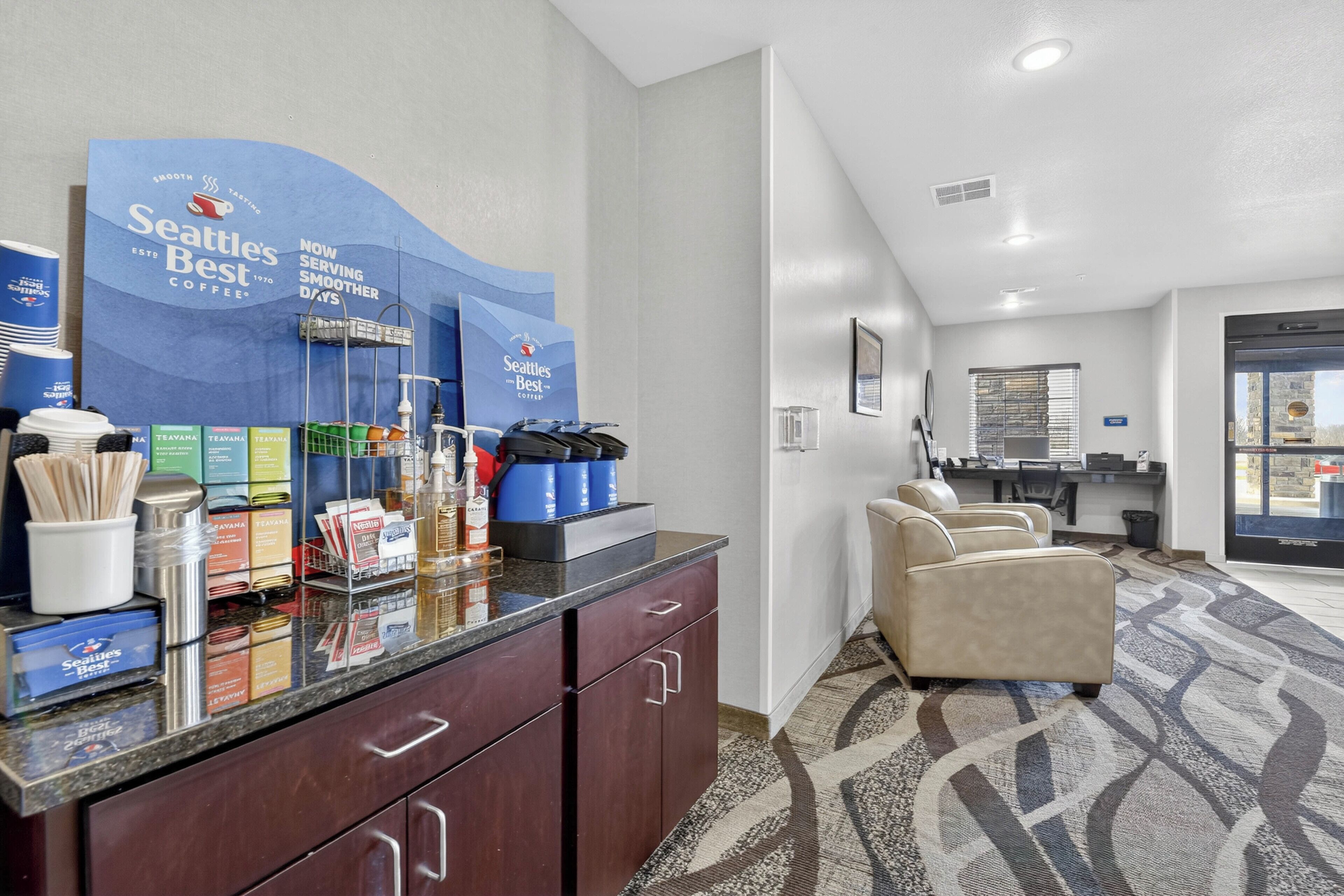 A hotel reception area with a coffee station, seating area, and a view of the city.