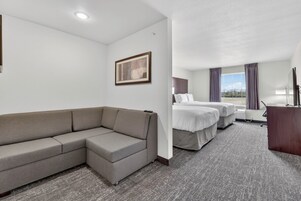 Habitación de hotel con sofá, dos camas, escritorio y ventana con cortinas.