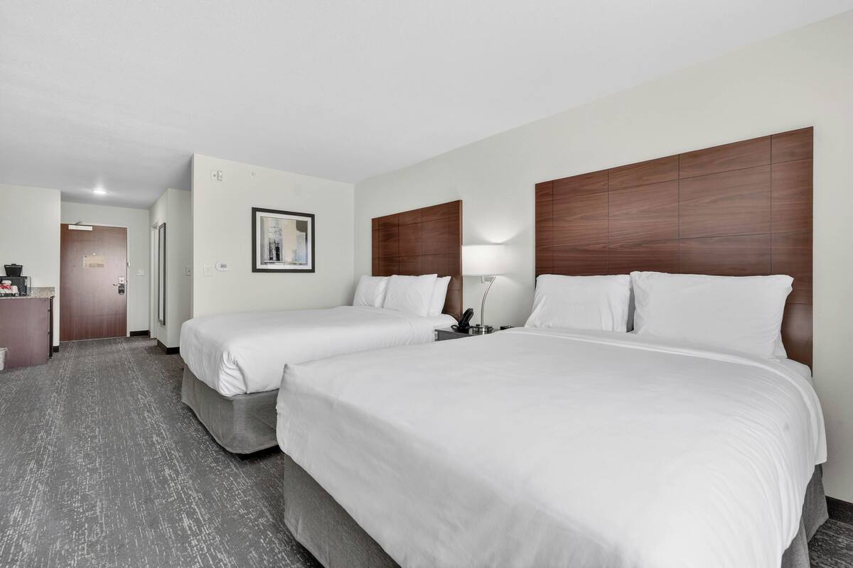 A hotel room with two beds, a desk, a chair, and a framed picture on the wall.
