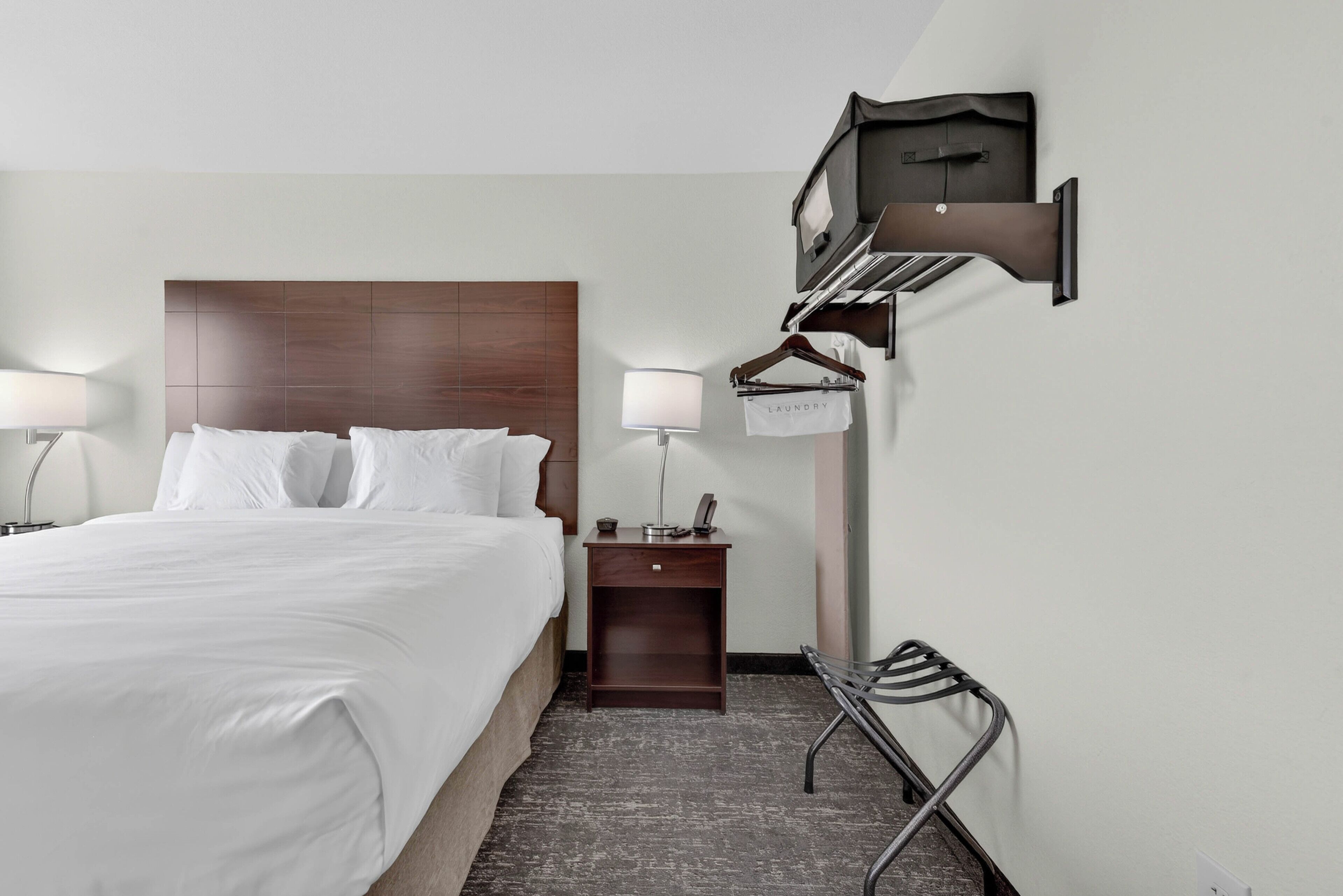 A hotel room with a bed, bedside lamps, a nightstand, a wall-mounted TV, and a coat rack.