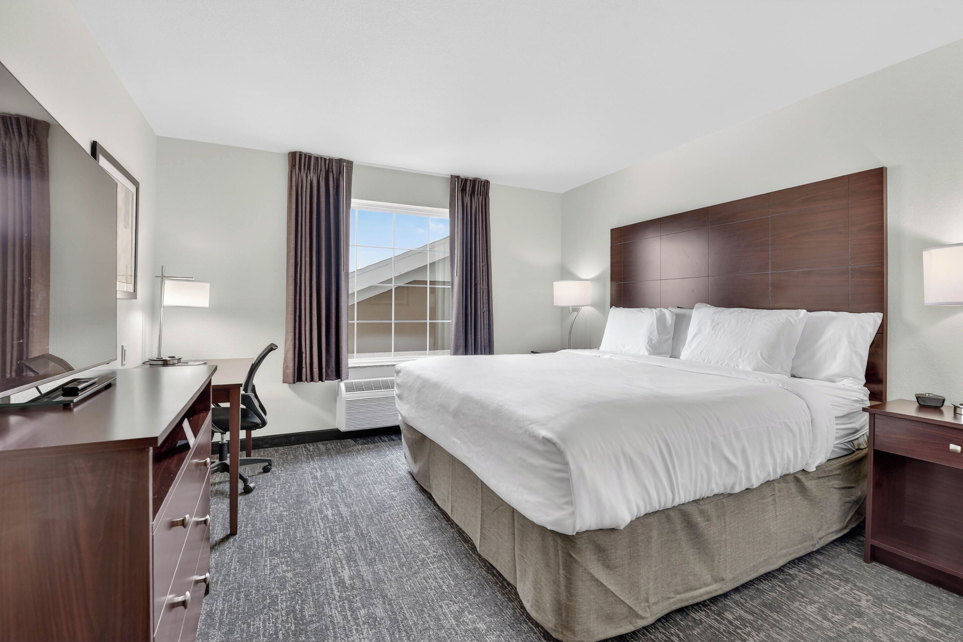 A hotel room with a bed, desk, chair, and a window with curtains.