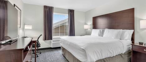 A hotel room with a bed, desk, chair, and a window with curtains.