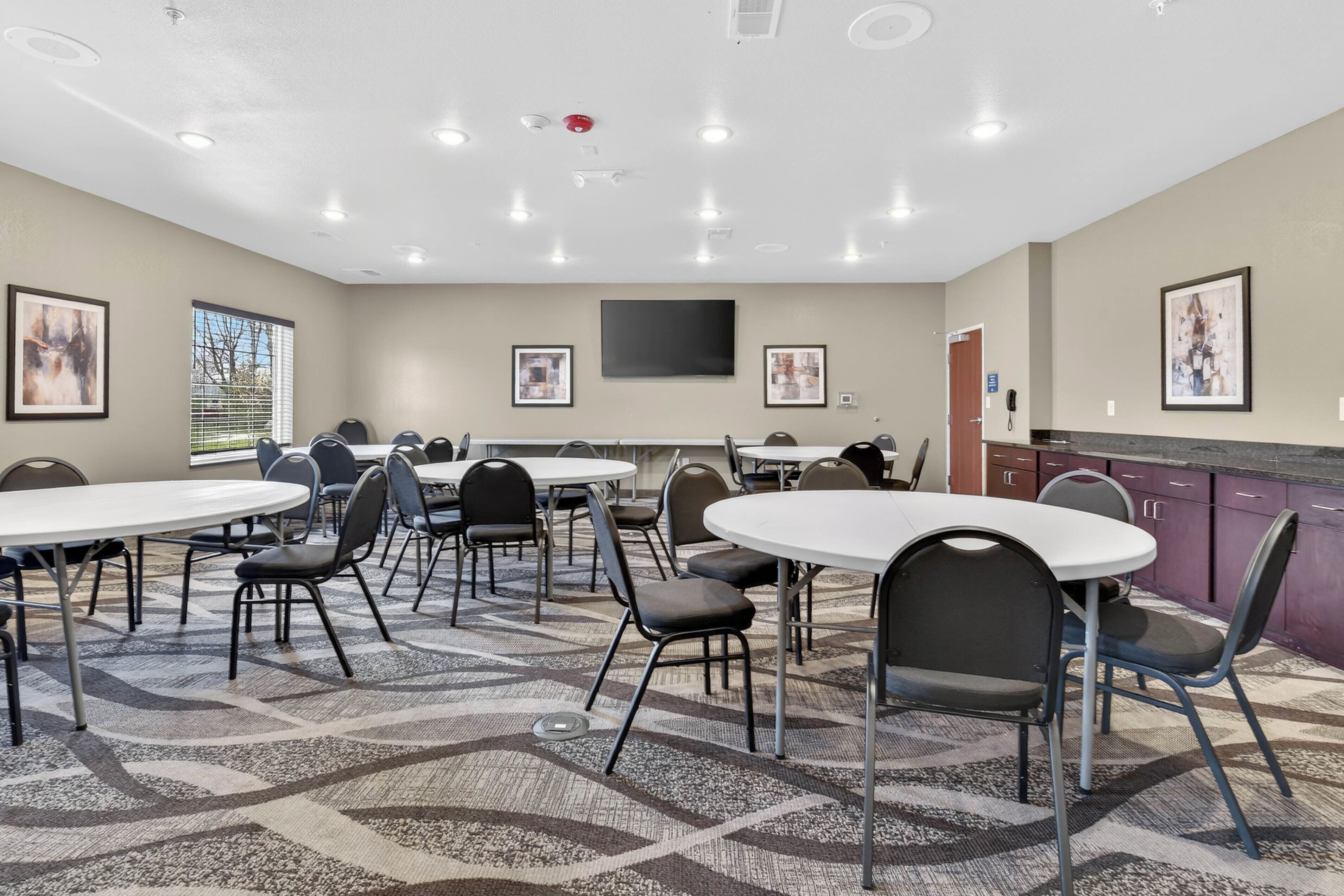 A conference room with round tables, chairs, a flat-screen TV, and framed artwork on the walls.