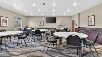 A conference room with round tables, chairs, a flat-screen TV, and framed artwork on the walls.