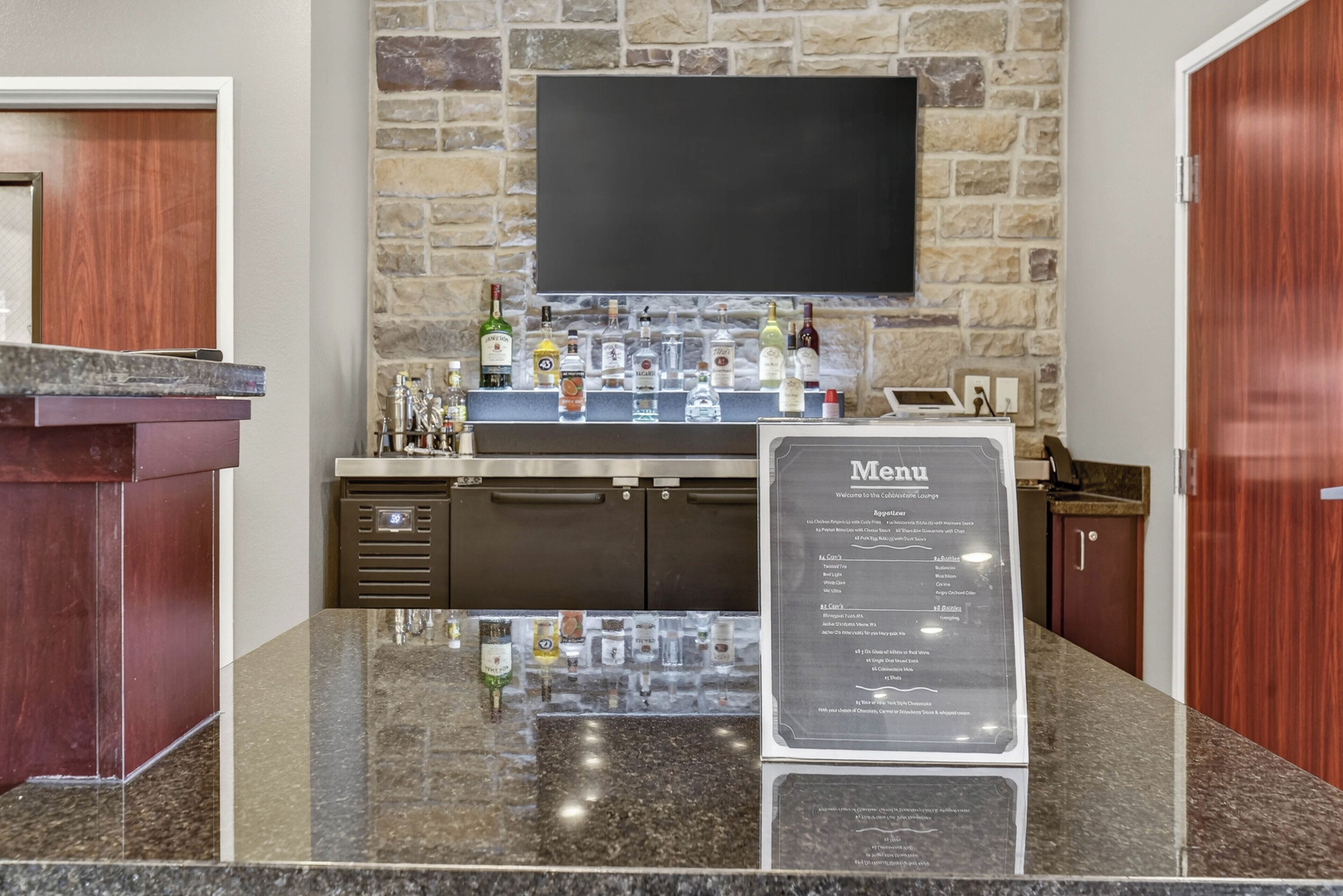 A bar area with a stone wall, a flat-screen TV, and a menu sign.